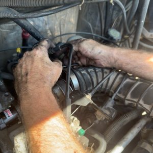 Technician's hands working on wiring and hoses inside an engine bay