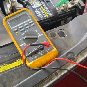 Technician testing an electrical circuit with a multimeter in the engine bay