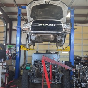 Ram heavy-duty truck on a lift with its engine and drivetrain lowered onto a floor jack below