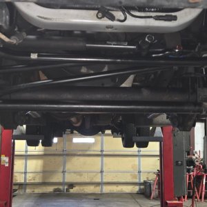 Underside view of a truck front axle and steering linkage while raised on a lift